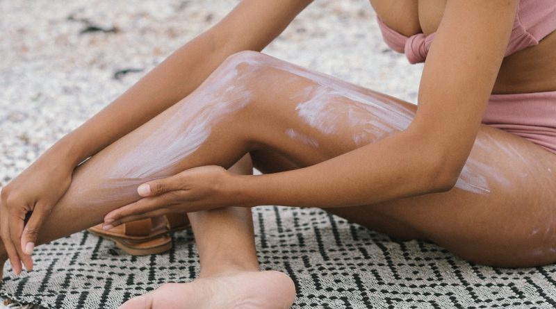 Une femme assise sur une textile en appliquant du crème solaire.