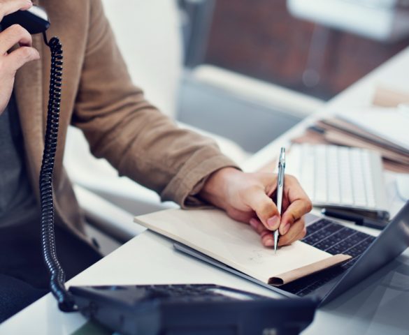 personne au téléphone en prenant des notes sur son carnet